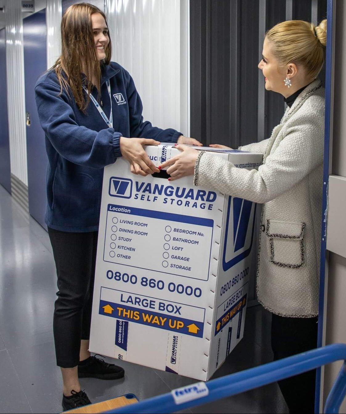 A photo showing a Vanguard employee helping a customer move some Vanguard cardboard boxes into one of the self-storage units.