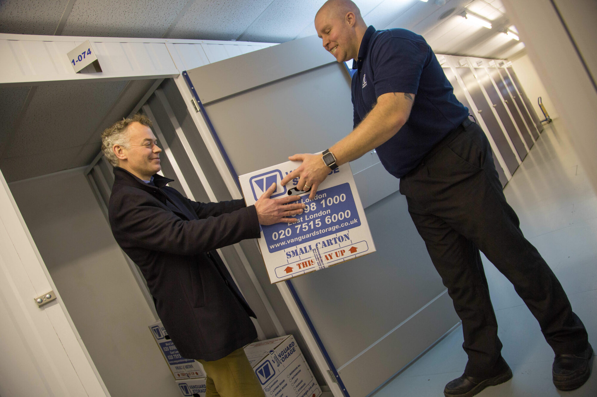 A photo showing a Vanguard employee helping a customer carry a Vanguard cardboard box into a self-storage unit.
