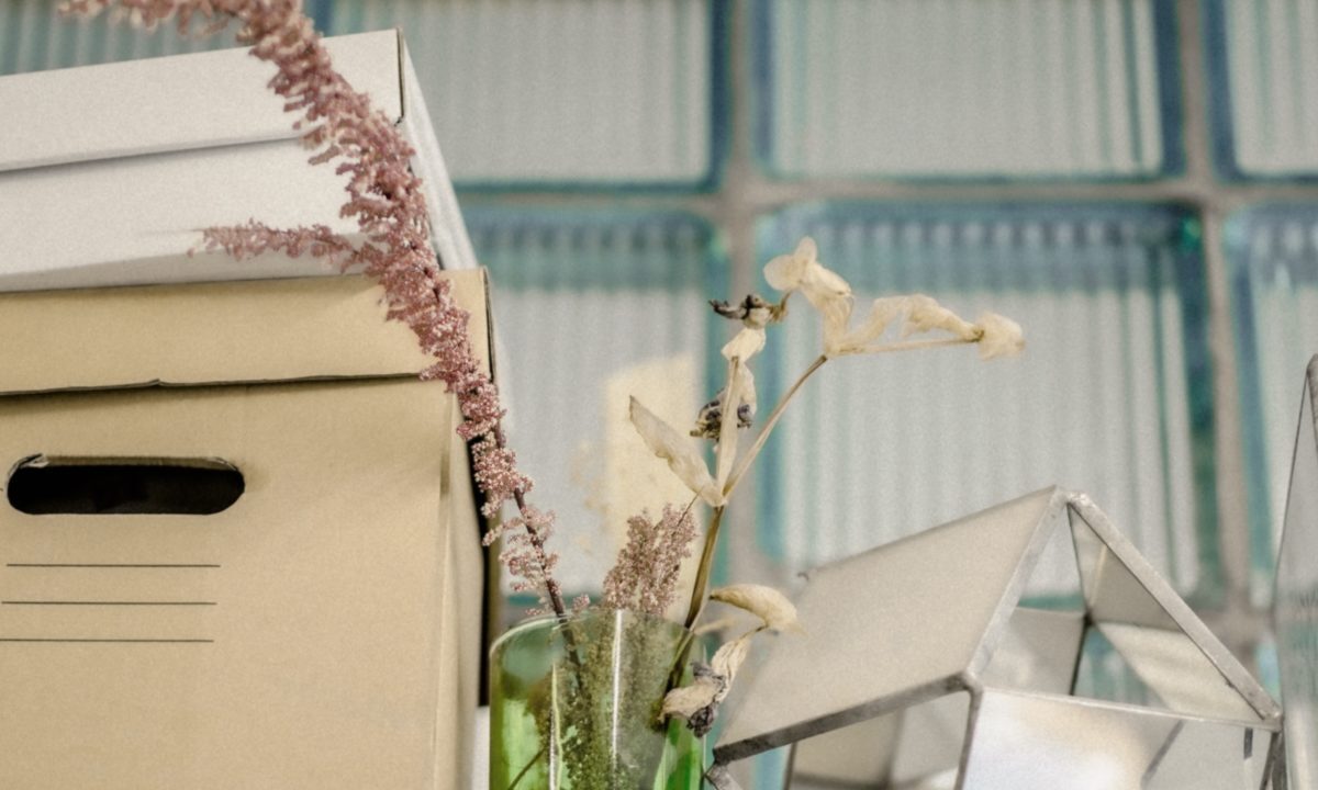 A photo showing a file storage box, some flowers in a vase and a smaller storage box on top.