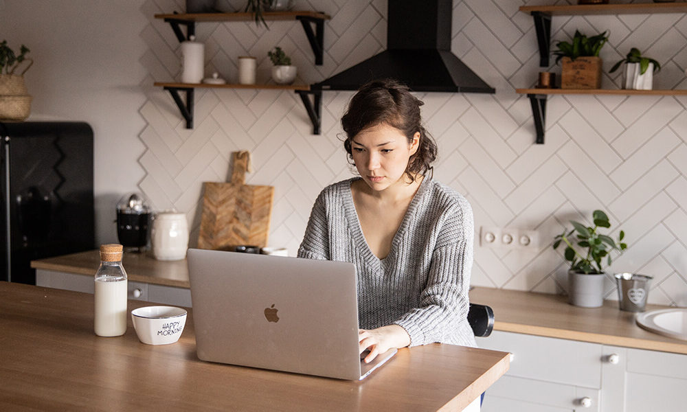 A photo showing a woman in front of a laptop in a kitchen.