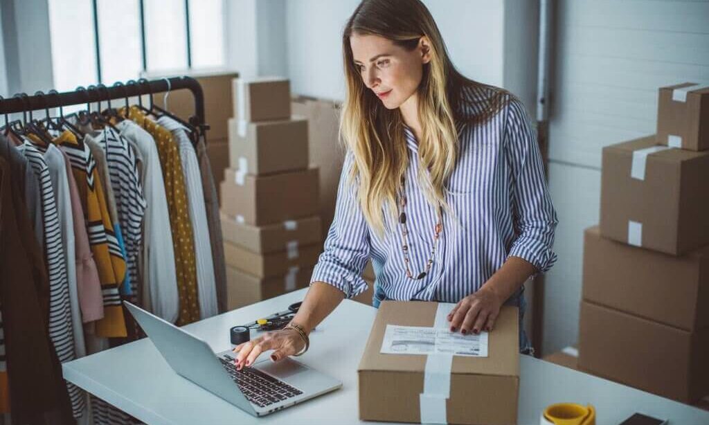 A photo showing a woman in front of a laptop while packing a parcel inside of a storage unit.