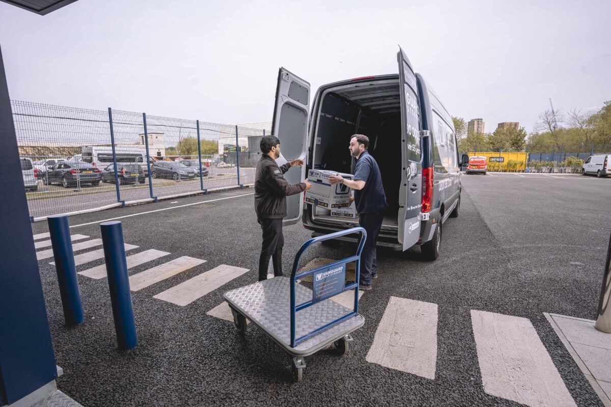 A photo showing a Vanguard employee helping a customer move boxes from a van and onto a trolley.