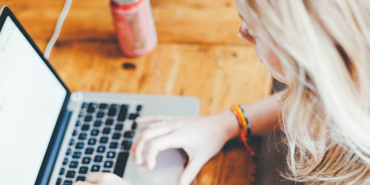 A photo showing a woman using her laptop with a soda can next to her.