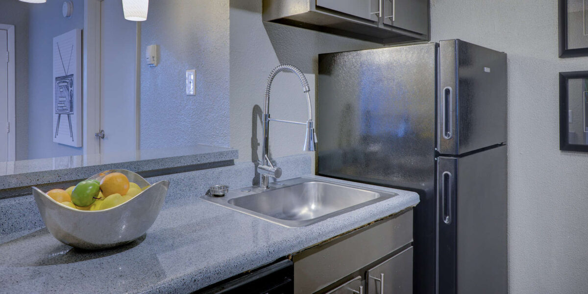 A photo of a kitchen with a fridge on the right and a fruit bowl on the counter on the left.