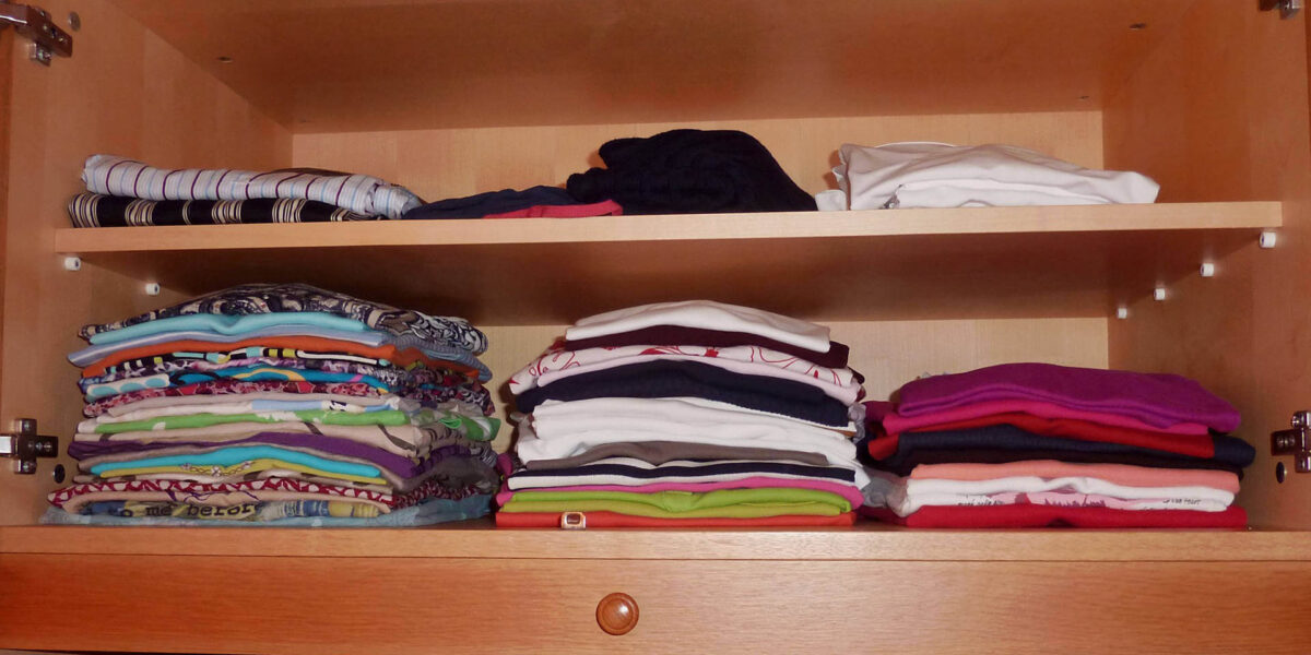 A photo showing the inside of a wardrobe with neatly folded t-shirts over two shelves.