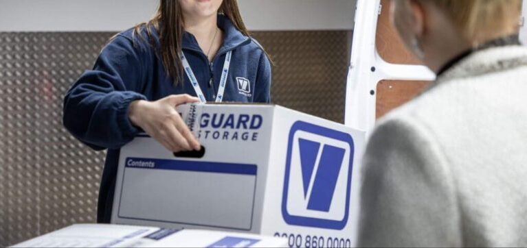 A photo showing a Vanguard employee carrying a Vanguard cardboard box for a customer.