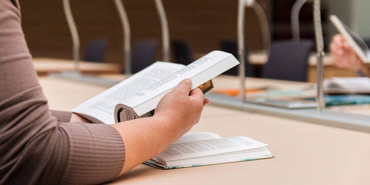 A photo showing a person reading a book at a library desk.