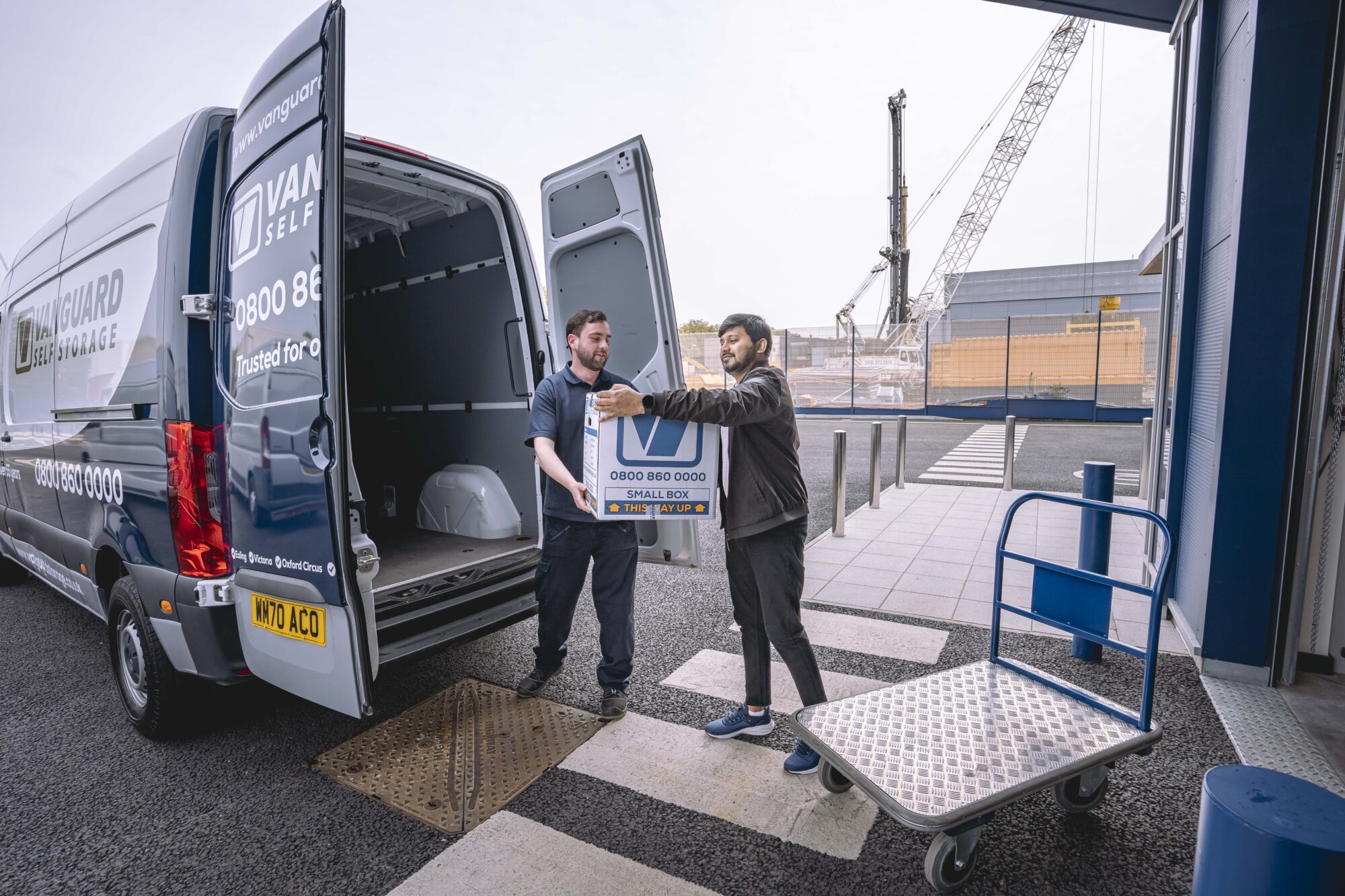 A photo showing a Vanguard employee helping a customer move boxes from a van and onto a trolley.