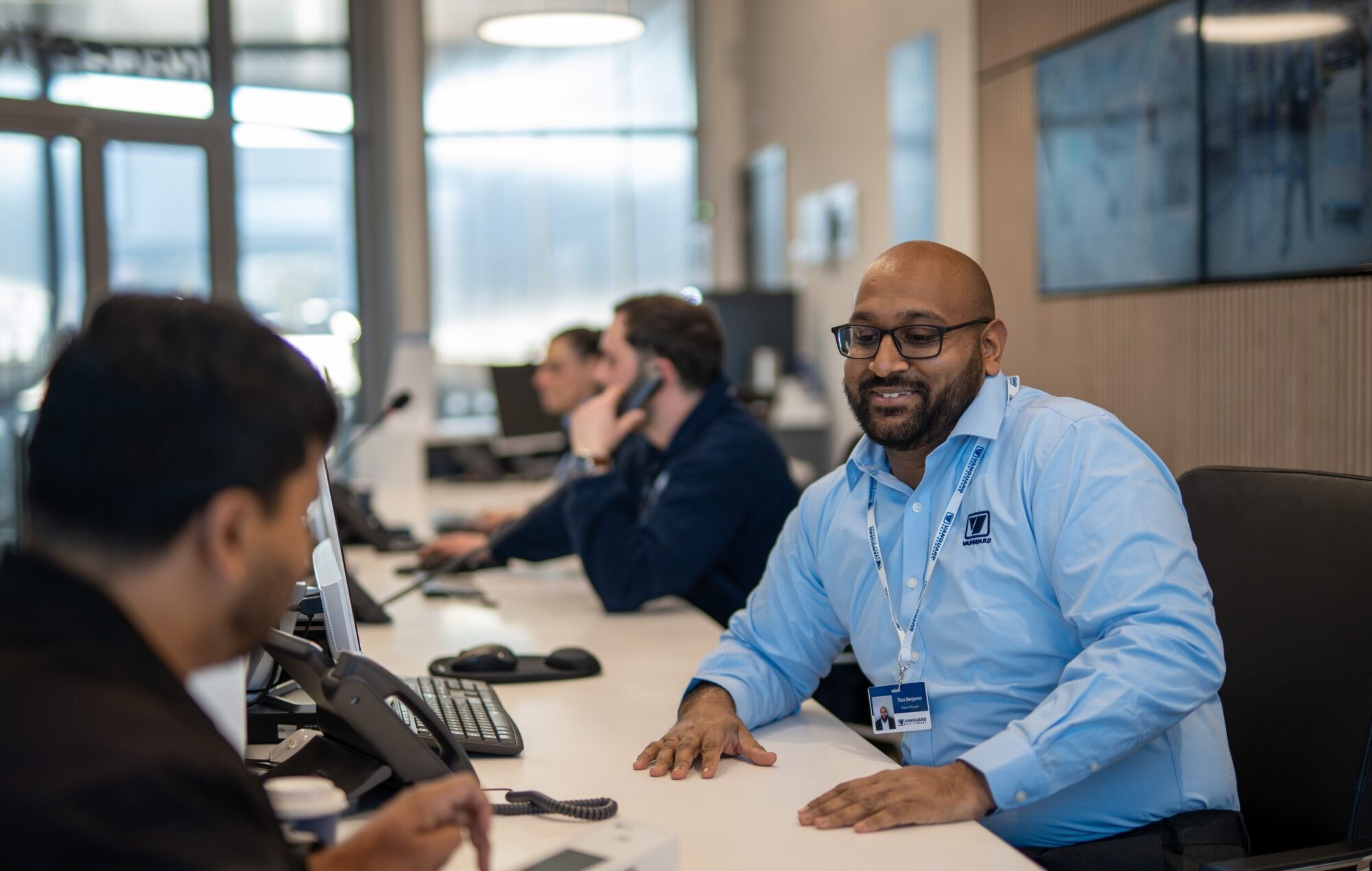 A photo of a Vanguard employee working at the reception and chatting to a customer.