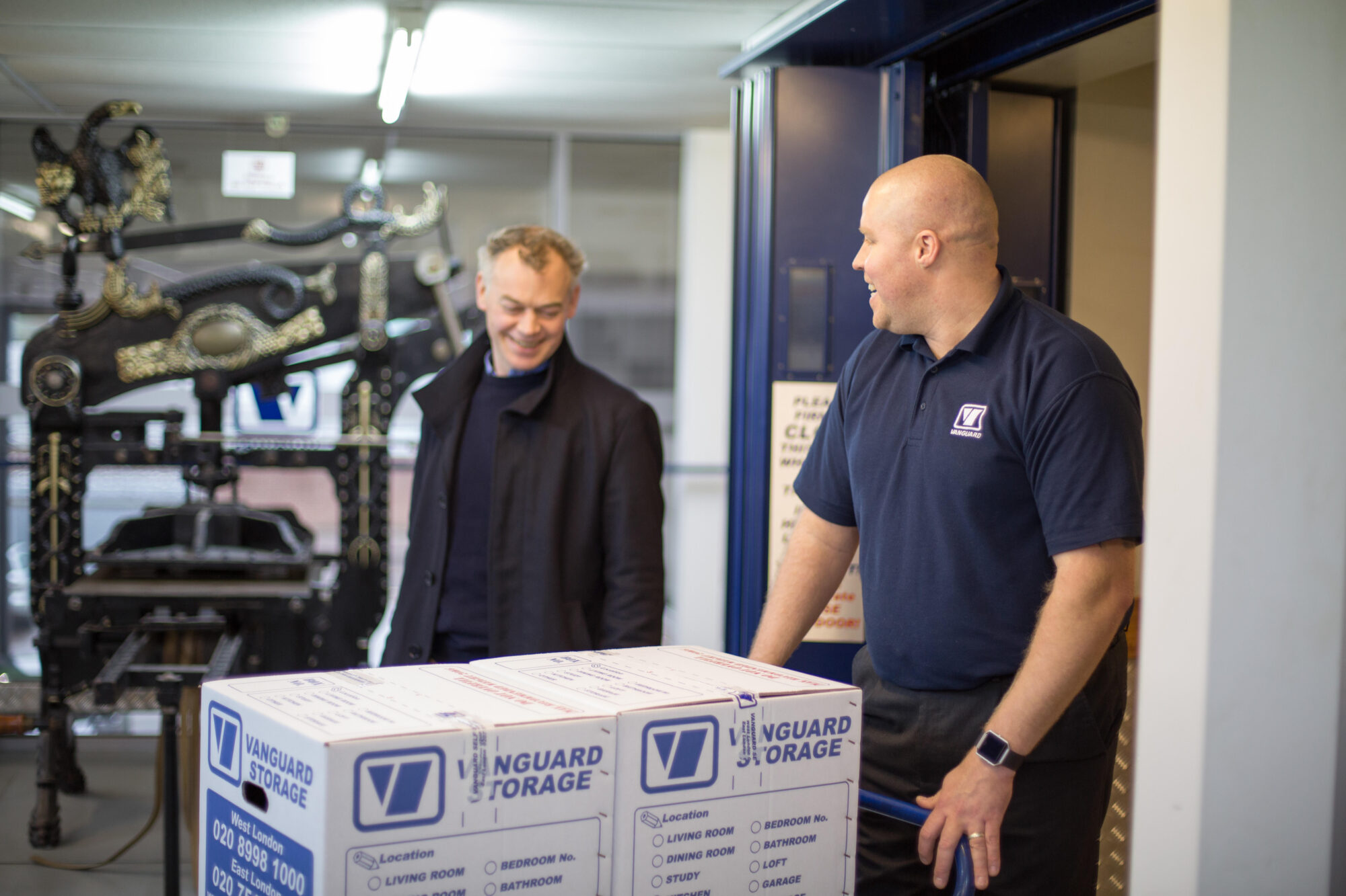 A photo showing a Vanguard employee helping a customer carry some Vanguard cardboard boxes into a self-storage unit.