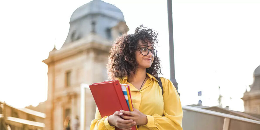 A photo of a student waring a backpack and holding a binder and notebooks.